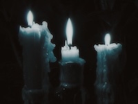 3 candles glowing blue in the darkness