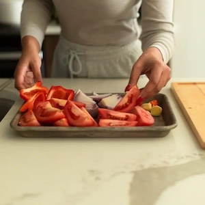 a person reaching for cut tomatoes and onions on a tray
